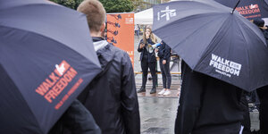 Zwei Personen mit einem Megaphon werden von Menschen umringt, die Regenschirme tragen mit der Aufschrift 