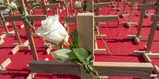 : Holzkreuze mit weissen Rosen stehen als Symbol fuer erfolgte Abtreibungen auf einem roten Stoff