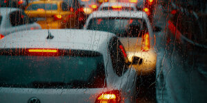 Die Rücklichter von Fahrzeigen, die im Stau stehen, fotografiert durch eine regennasse Windschutzscheibe