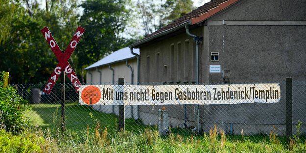 Ein Transparent mit der Aufschrift ?Mit uns nicht! Gegen Gasbohren Zehdenick/Templin? hängt an einem Zaun neben einem roten Holzkreuz mit der Aufschrift ?No Gas?.