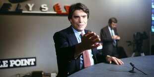 Tapie in einem Fernsehstudio am Tisch mit einem kleinen Mikrophon