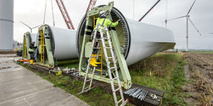 Zwei Arbeiter stehen auf einer Leiter und montieren an einem Teil einer Windturbine