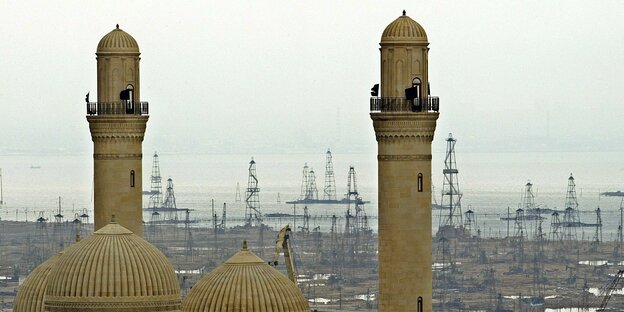 Türme einer Moschee im Voprdergrund und Ölbohrtürme im Hintergrund