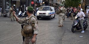 Männer in Tarnfleckuniformen regeln den Straßenverkehr, ein Krankenwagen fährt vorbei