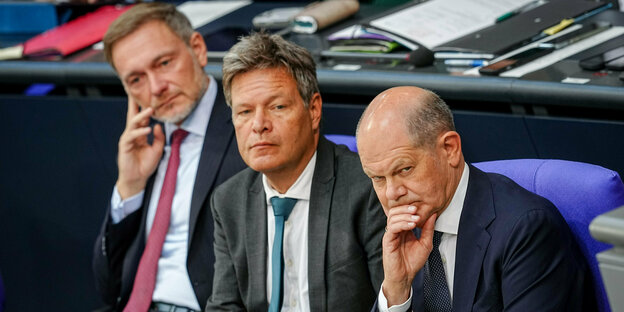 Christian Lindner, Robert Habeck and Olaf Scholz sit on the government bench with wrinkled faces.