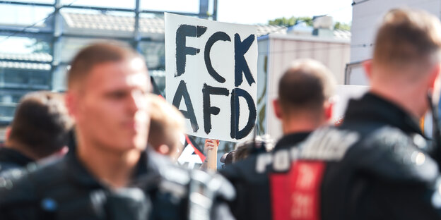 Polizisten stehen bei Demo: Einer hält ein Plakat hoch mit der Forderung: FCK AFD