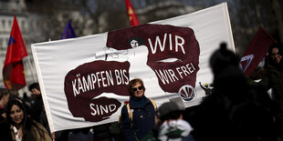 Demonstrierende halten ein Protestschild mit der Aufschrift: 'Wir kämpfen bis wir frei sind', in die Höhe.