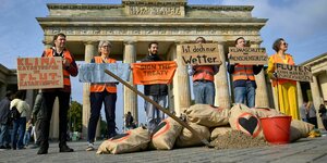 Mitglieder der "Letzten Generation" stehen mit Plakaten und Sandsäcken vor dem Brandenburger Tor und protestieren gegen den Klimawandel.