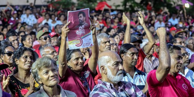 Wahlkampfveranstaltung in Sri Lanka, viele Menschen schauen aufmerksam, jemand hält ein Plakat mit dem Bild des Präsidentschaftskandidaten in den Händen