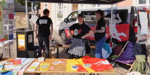 Drei junge Menschen stehen vor einem Auto an einem Stand mit Informationsbroschüren