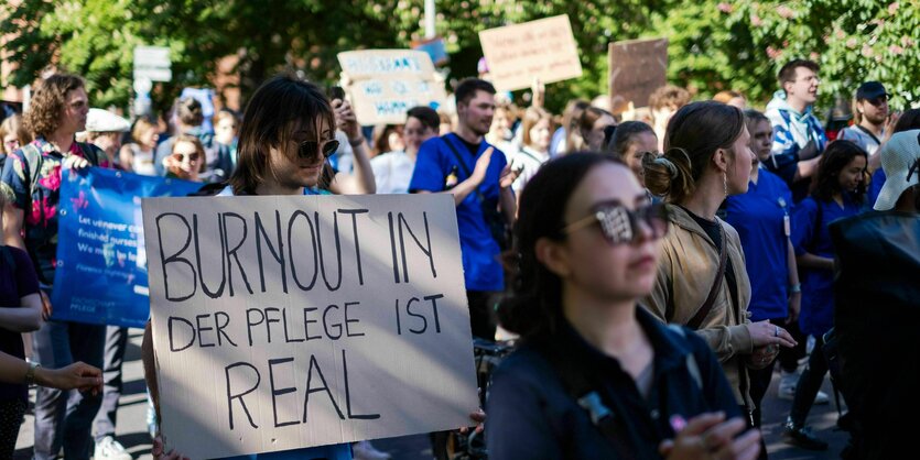 Protestaktion, vor allem jüngere Menschen stehen auf einem Platz und halten Plakate hoch: Burnout in der Pflege ist real