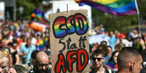 Demonstration mit Regenbogenfahne und Plakat mit der Aufschrift 