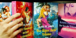 eine Hand greift nach einem von mehreren Büchern in einem Regal, Titel: 