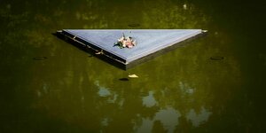 Auf einem Dreieck in der Wasserfläche des Denkmals für die ermordeten Sinti und Roma liegt eine Rose