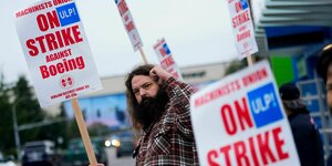 Ein Mann mit Bart hebt die Faust. Er hält ein Schild, auf dem steht: "Im Streik gegen Boeing"