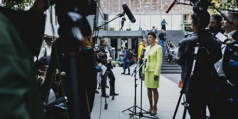 Wagenknecht im gelben Kostüm zwischen Mikrofonen