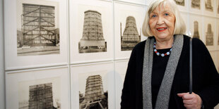 Eine Frau mit grauen Haaren steht vor einer Wand mit Fotografien von Kühltürmen