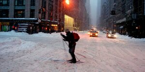 Eine Person mit Skiern auf einer Straße in New York im Schnee.