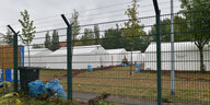 Hinter einem Zaun sind weiße Zelte zu sehen