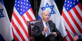 Joe Biden sitzt vor einer Reihe von US- und Israelfahnen