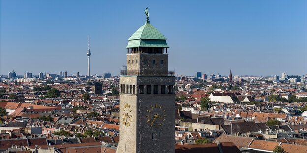 Das Bild zeigt den steinernen Turm des Rathhauses Neukölln, an dem eine Uhr befestigt ist.