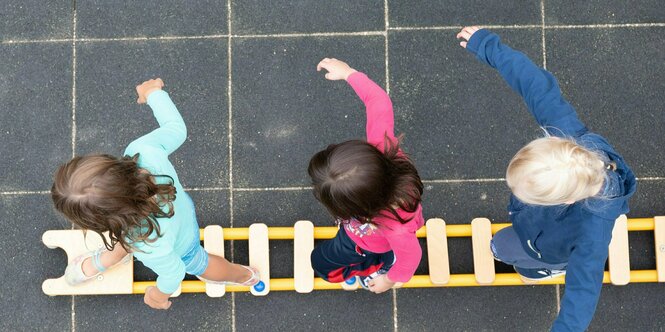 Kinder balancieren während eines Pressetermins auf dem Spielplatz einer Kindertagesstätte auf einem Brett