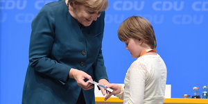 Angela Merkel überreicht einem Kind eine Autogrammkarte.