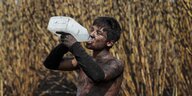 Ein Mann steht in einem Zuckerrohrfeld und trinkt Wasser aus einer Plastikflasche