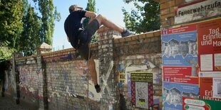 Das Bild zeigt die Mauer rund um den Görlitzer Park. Ein Mann klettert gerade über die Mauer