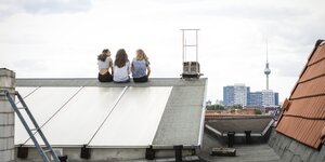 Drei Meenschen sitzen in Berlin auf einem Dach mit Solaranlage