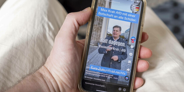 Eine Hand hält ein Mobiltelefon auf dessen Display ein Video des AFD Politikers Max Krah zu sehen ist