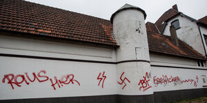 An einer weißen Hauswand sind in roter Farbe die Worte „Raus Hier" und Hakenkreuze geschmiert