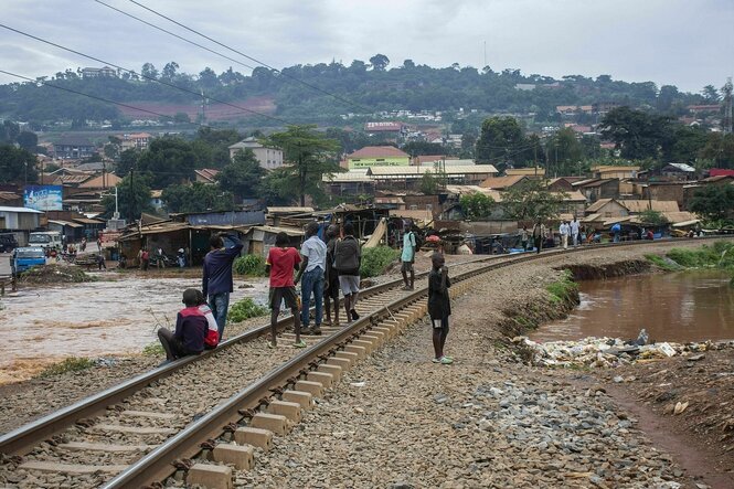 Eine Gruppe steht auf Bahngleisen, das Wetter ist trübe, es stehen Pfützen in der Landschaft