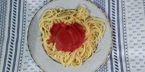 Ein Teller Spagetti auf einem Tisch mit gemusteter Tischdecke