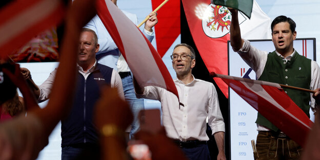 Herbert Kickl und Mitglieder der FPÖ stehen bei einer Wahlkampfveranstaltung auf einer Bühne und schwenken Fahnen