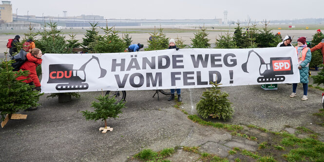 Hände weg vom Feld steht auf einem Banner neben gebrauchten Weihnachtsbäumen auf dem Tempelhofer Feld