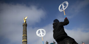 silberne Peacezeichen werden in den Himmel gereckt vor der goldenen Siegessäule