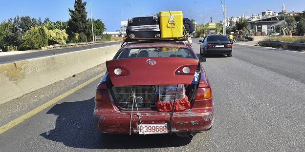 Ein voll beladenes rotes Auto fährt auf einer vierspurigen Straße