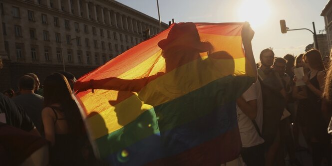 Silhouetten von mehreren Personen hinter einer Regenbogenfahne