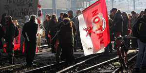 Demonstranten mit einer großen Fahne auf Bahngleisen