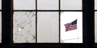 Blick durch eine zerbrochene Fensterscheibe auf die US-Fahne