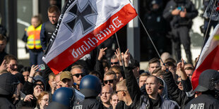 Menschen mit einer Reichsflagge zeigen ihre Mittelfinger in Richtung von behelmten Polizisten.