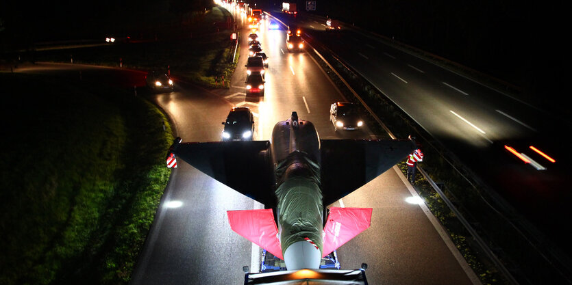 Ein Kampfflugzeug wird nachts auf einer Autobahn transportiert.