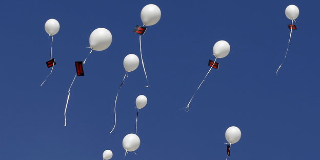 Weiße Luftballons, an die Namensschilder geheftet sind, fliegen in den blauen Himmel