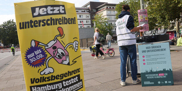 Eine Person steht vor einem Plakat mit der Aufschrift "Hier drucken und unterschreiben".