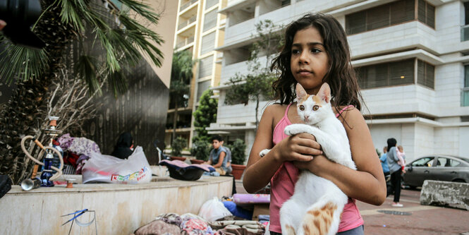 Ein neunjähriges Mädchen hält ihre Katze vor die Brust. Hinter ihr ein Matratzenlager auf der Straße in Beirut.