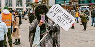 Eine Person in Parka und mit maskiertem Gesicht trägt ein Schild mit der Aufschrift "Wir haben es satt" und fotografiert mit dem Handy die Fotografin