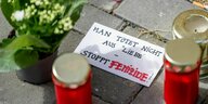 Blumen und Kerzen liegen nach einem tödlichen Messerangriff vor einem Hauseingang in Berlin-Friedrichsfelde neben einem Zettel mit der Aufschrift „Man tötet nicht aus Liebe - Stoppt Femizide“.