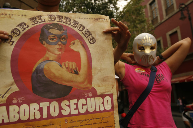 Eine Frau mit einer Wrestlingmaske neben einem Schild „Aborto securo“