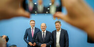 Christian Lindner, Olaf Scholz und Robert Habeck werden mit einem Smartphone fotografiert